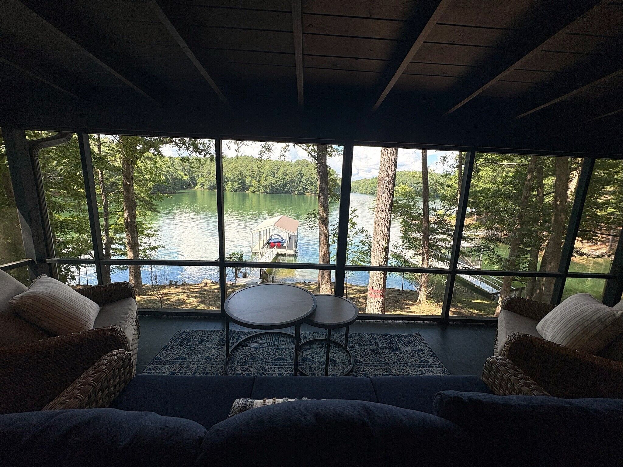 A room with a large window overlooking a lake, a small round table, and two wicker sofas.