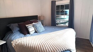 A bedroom with a bed, pillows, a nightstand, a lamp, and a window with curtains.