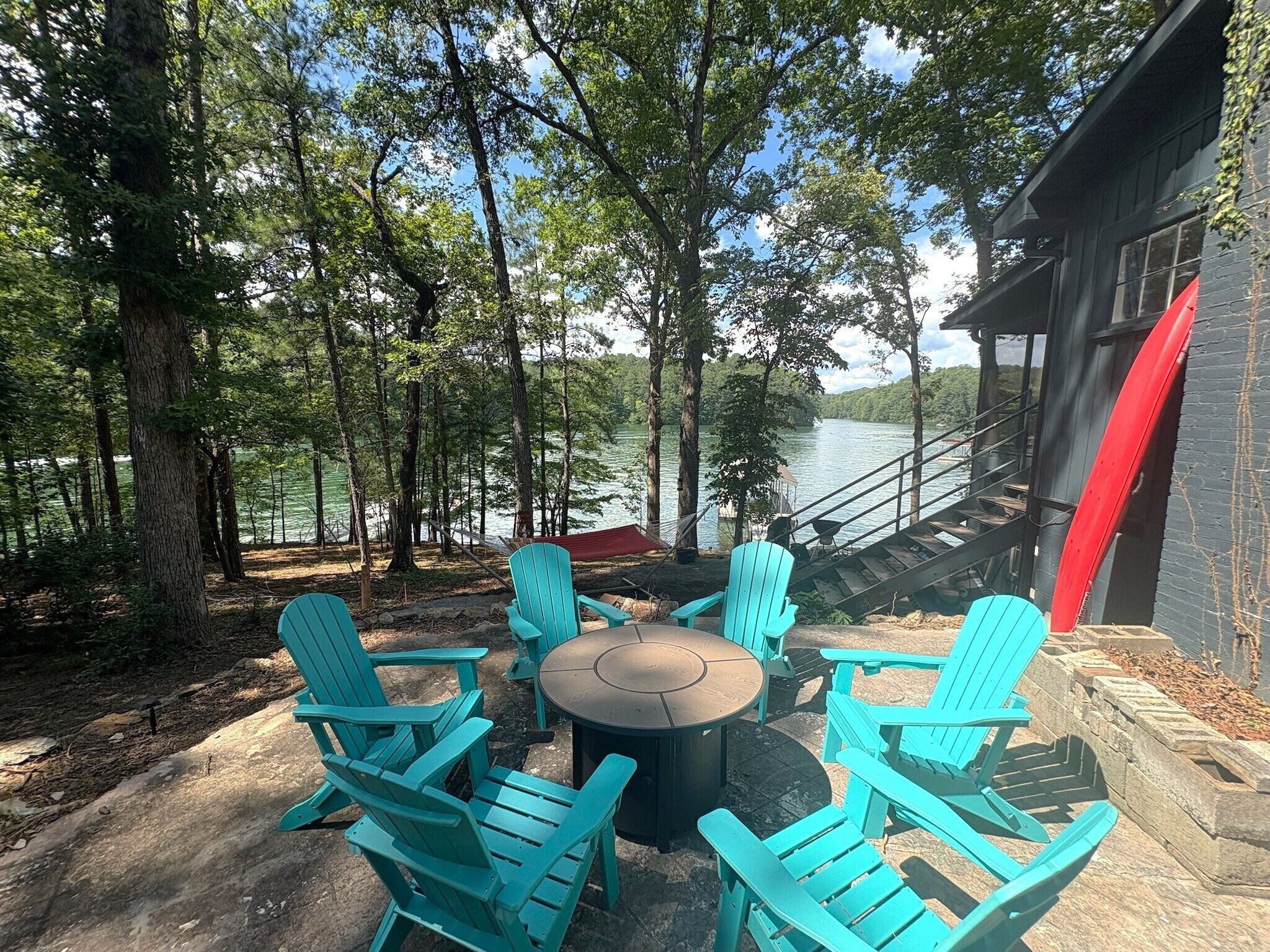 An outdoor seating area with chairs and a table, surrounded by trees and overlooking a body of water.