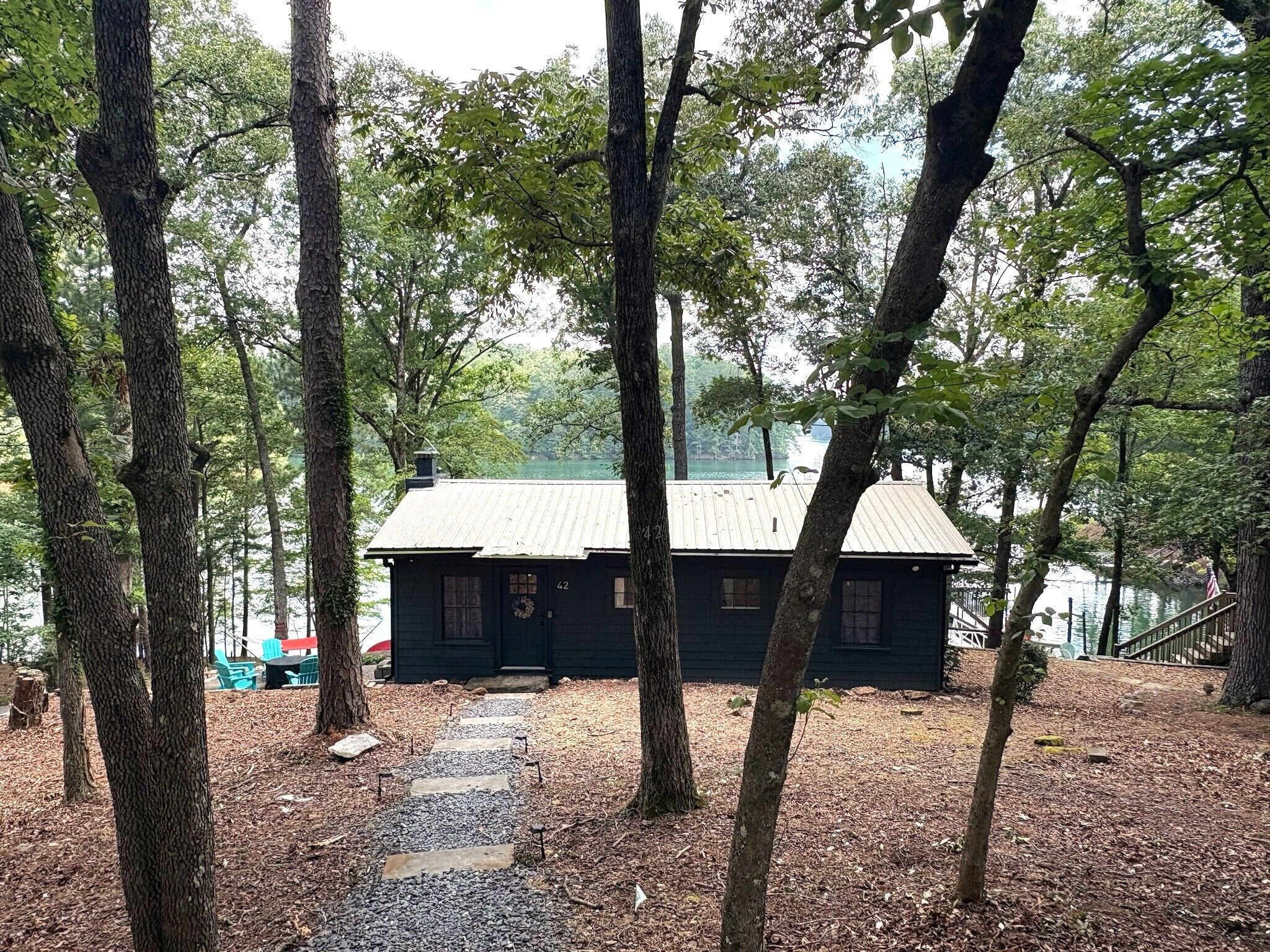 A cabin with a metal roof, surrounded by trees and a gravel path leading to it.