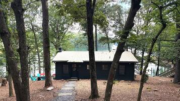 A cabin with a metal roof, surrounded by trees and a gravel path leading to it.