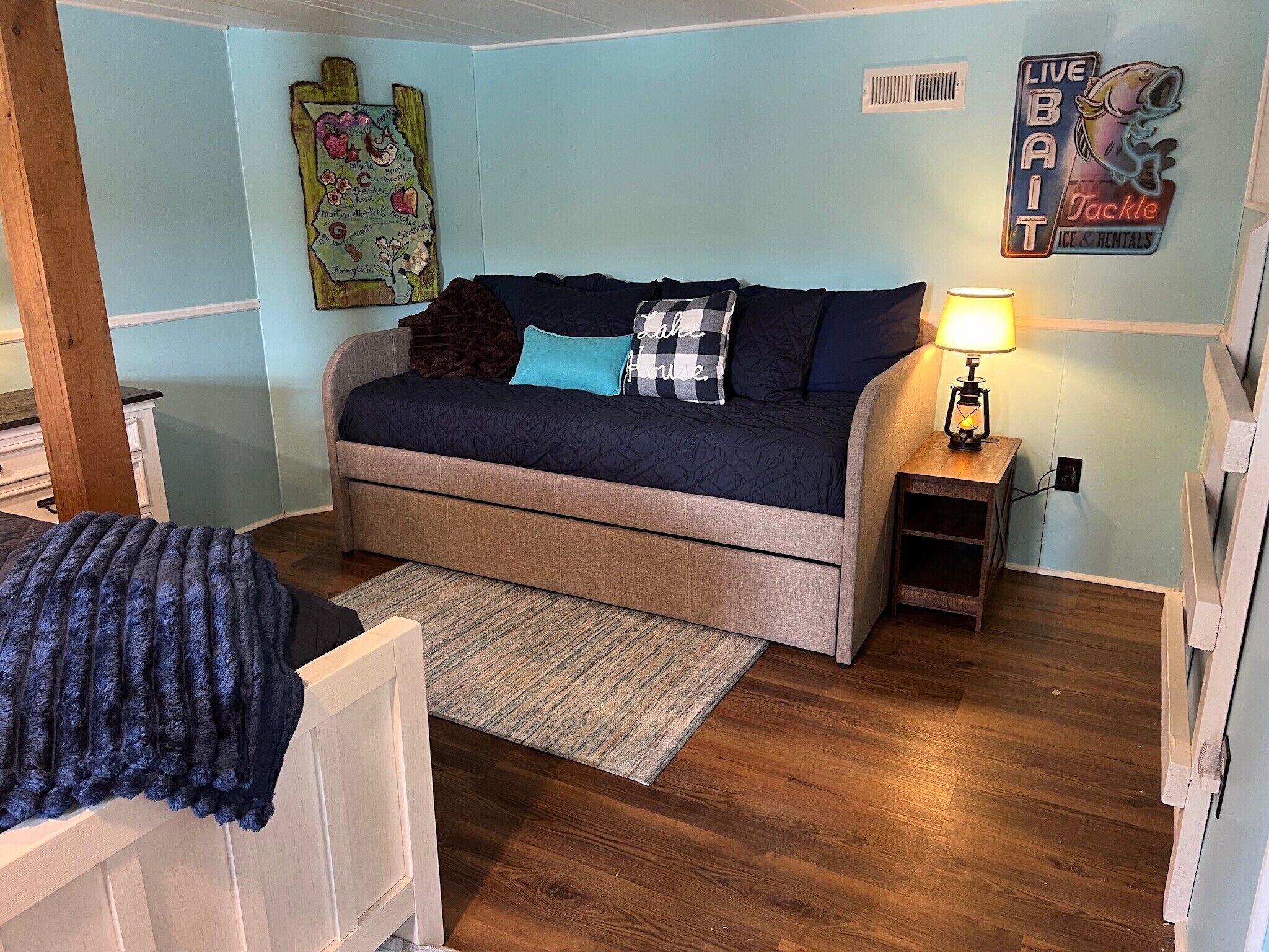 A bedroom with a bed, a nightstand, a lamp, a wall art piece, and a sign.