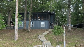 A wooden bridge leading to a modern cabin surrounded by trees.