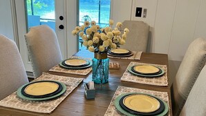 A dining table set with plates and a vase of flowers, chairs around it, and a view of the outdoors through a door.