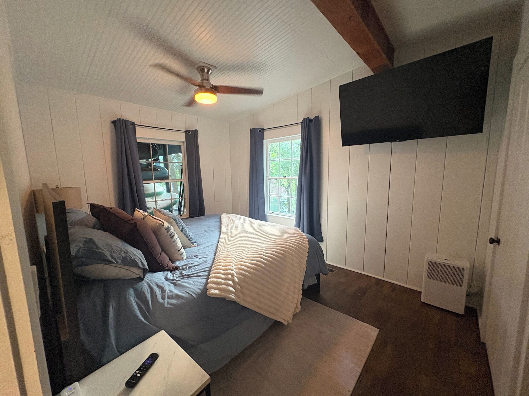 A bedroom with a bed, a ceiling fan, a mounted TV, and a window with curtains.