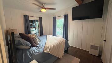 A bedroom with a bed, a ceiling fan, a mounted TV, and a window with curtains.