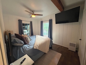 A bedroom with a bed, a ceiling fan, a mounted TV, and a window with curtains.