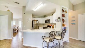 A modern kitchen with white cabinetry, a central island with two barstools, a microwave, and a refrigerator. - 3-bedroom house in peaceful Melbourne with cool AC (Melbourne)