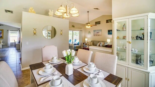 A dining area with a wooden table set for four, a white cabinet with glass doors, and a ceiling fan. - 3-bedroom house in peaceful Melbourne with cool AC (Melbourne)