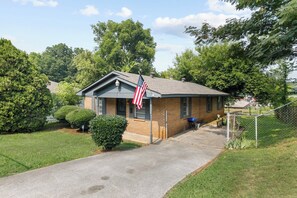 A small brick house with a front porch, an American flag, and a blue grill outside. - 32nd Street Retreat | Downtown/Backyard/Parking (Birmingham)