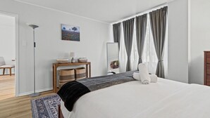 Une chambre d’hôtel avec un lit, une table de chevet avec une lampe, un miroir et une fenêtre avec des rideaux.