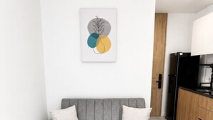 Un canapé gris avec des coussins, un meuble en bois et un coin cuisine avec un réfrigérateur noir.