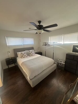 Une chambre à coucher comprenant un lit, des tables de chevet, un ventilateur de plafond et une commode.