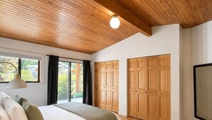 A bedroom with a wooden ceiling, a bed with pillows, a bedside table, and a large window. - Mountain Escape | Sauna & Outdoor fire Pit (Squamish)