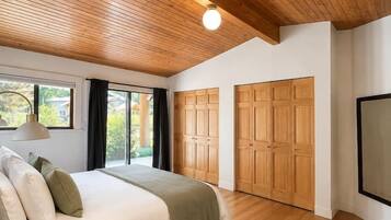 A bedroom with a wooden ceiling, a bed with pillows, a bedside table, and a large window.