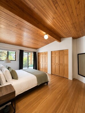 A bedroom with a wooden ceiling, a bed with pillows, a bedside table, and a large window.