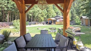 An outdoor wooden deck with a table and chairs, a grill, and a pergola structure. - Mountain Escape | Sauna & Outdoor fire Pit (Squamish)