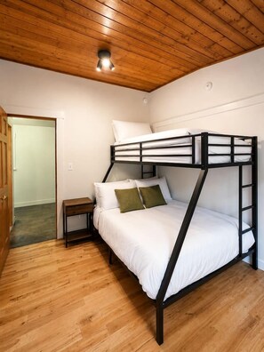 A bunk bed with a wooden ceiling and a small bedside table.