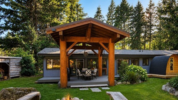 Ein hölzerner Pavillon mit Feuerstelle, Gartenmöbeln und einer überdachten Terrasse.