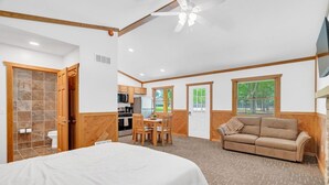 A bedroom with a bed, a dining area with a table and chairs, a sofa, and a kitchen in the background. - Whitetail Ridge Cabins | Three Cabin Retreat (Lexington)