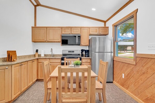 A compact kitchen with wooden cabinets, a stainless steel refrigerator, a microwave, and a dining area with a table and chairs.