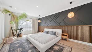 A modern bedroom with a large bed, wooden paneling, a hanging light, and a potted plant. - Coastal Retreat / Near 30A / Pool / 4BR / Sleeps 10 (Santa Rosa Beach)