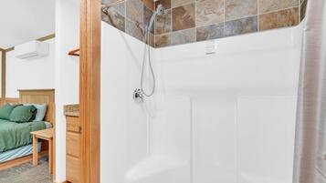 Une salle de bain avec douche, un lit en bois et une petite table.