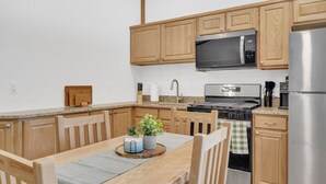 A compact kitchen with wooden cabinets, a stainless steel stove, a microwave, and a refrigerator.