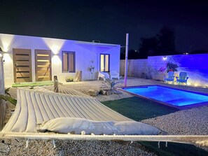 A modern outdoor pool area with a hammock, a small deck, and a house with illuminated windows. - Curaçao Retreat with Pool & AC - 9min/ Beaches. (Willemstad)