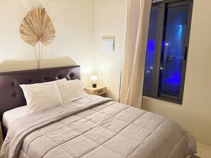 A bed with a headboard, a bedside lamp, a window with curtains, and a wall-mounted decorative piece. - Curaçao Retreat with Pool & AC - 9min/ Beaches. (Willemstad)