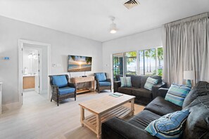 A living room with a sofa, chairs, a coffee table, a painting, and a view through large windows.