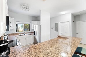 A modern kitchen with white cabinets, granite countertops, stainless steel appliances, and a large island. - Kai-Tastic 15B - 2BR Kaibo Condo with Pool and Beach (Rum Point)
