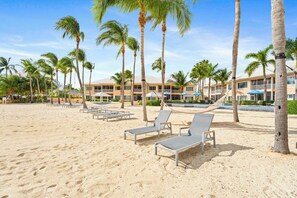 A beach resort with palm trees, lounge chairs, and a building with balconies.