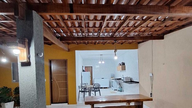 Un espacio exterior cubierto con un banco de madera, piso de baldosas y vista hacia una cocina.