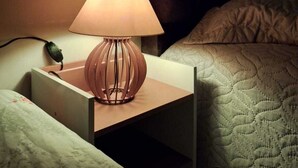 Una mesita de noche con una lámpara, un enchufe y un pequeño dispositivo electrónico.