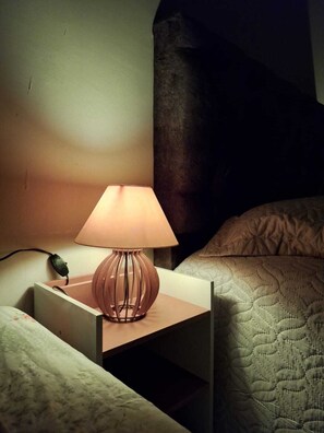 A bedside table with a lamp, a power outlet, and a small electronic device on it.