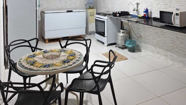 Cocina compacta con paredes de azulejos blancos, estufa a gas, microondas y un mueble de madera sobre la encimera.