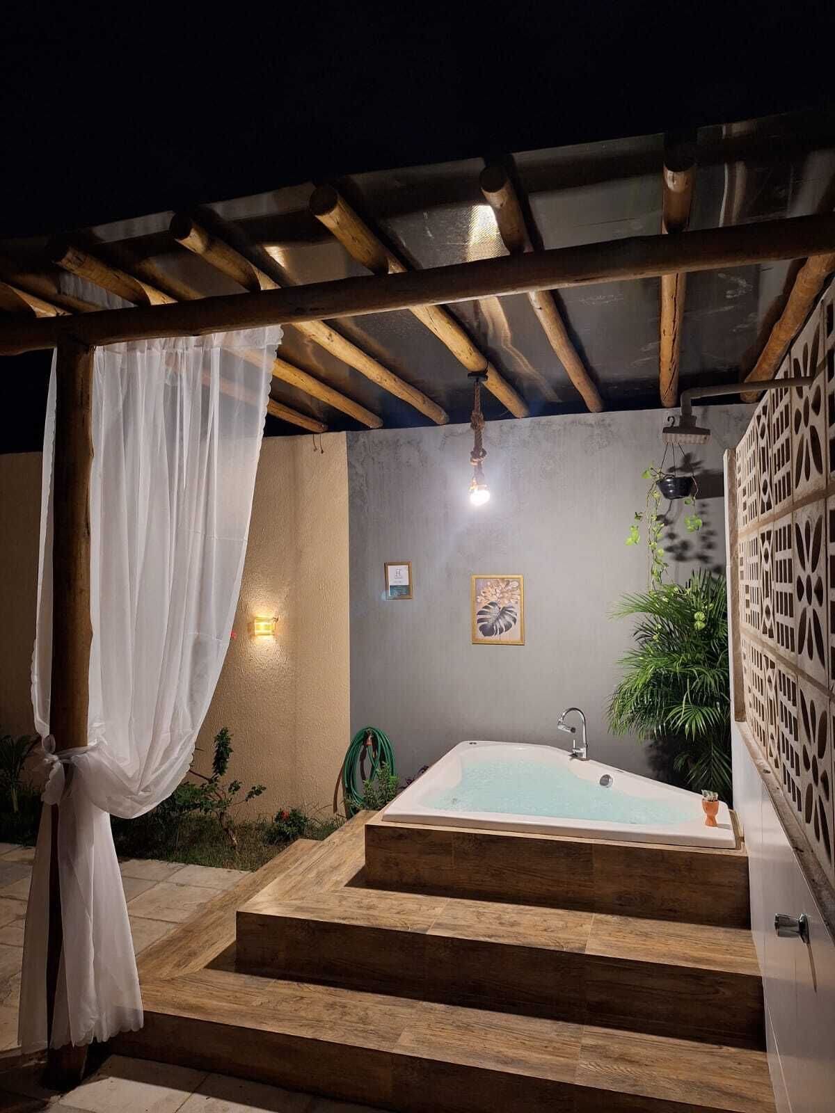 Uma área de spa ao ar livre com pergolado de madeira, uma banheira branca e um pequeno jardim.