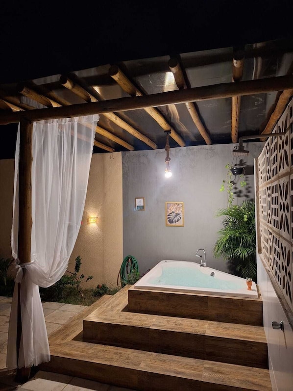 An outdoor spa area with a wooden pergola, a white bathtub, and a small garden. - Chácara Recanto do Sítio (Barbalha)