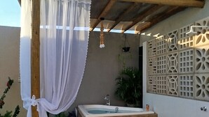 Un área de spa con terraza de madera, un jacuzzi y una pérgola con cortinas blancas.