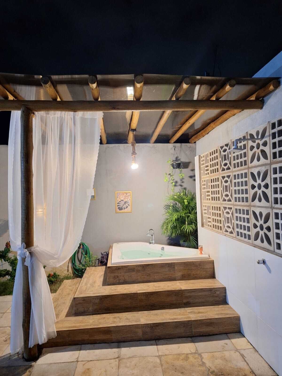 A private outdoor bathroom with a wooden bathtub, steps leading up to it, and a pergola with a white canopy.