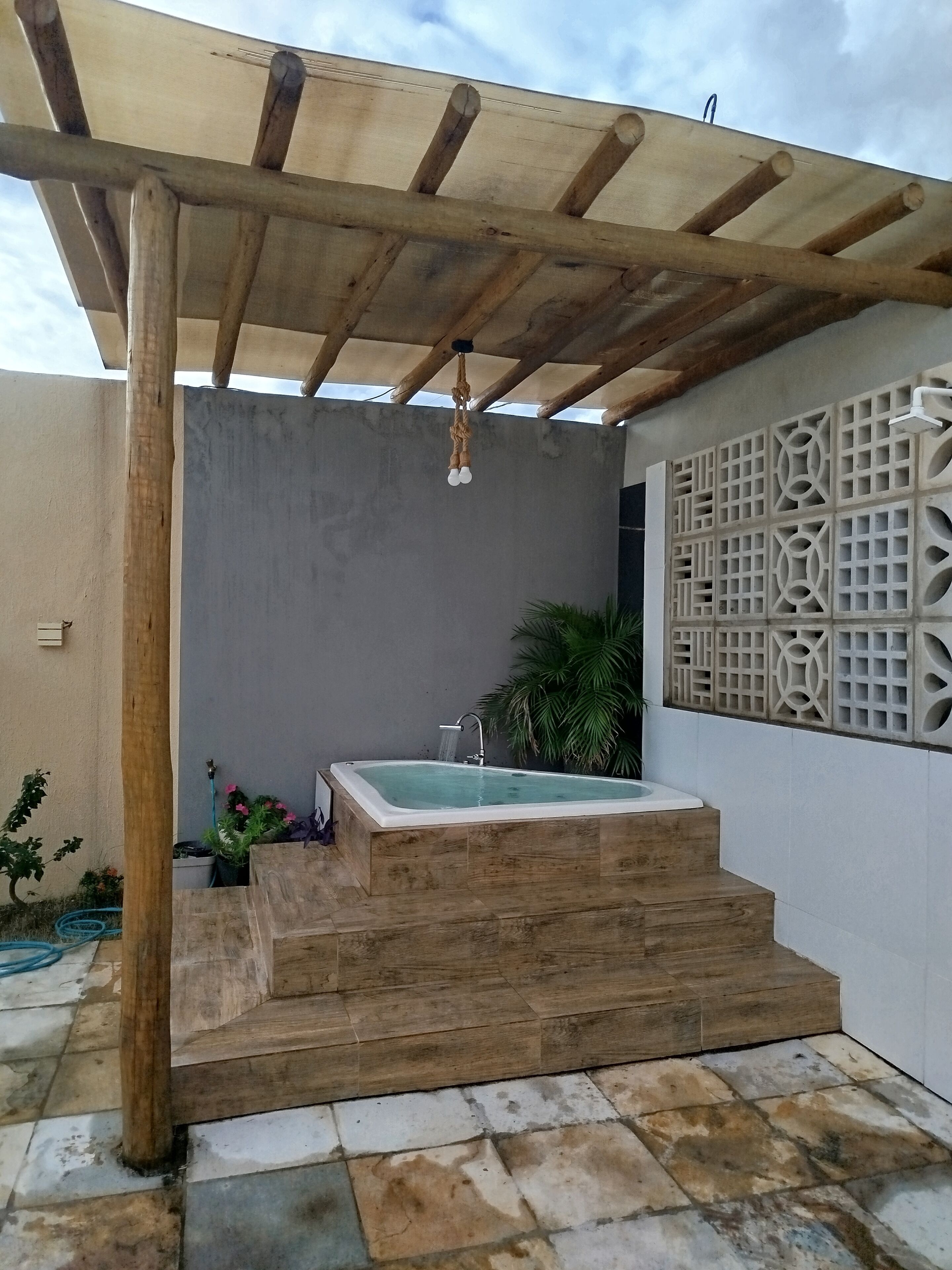 Zona de spa con hidromasaje, escalones de madera, una pérgola y una pared decorativa.