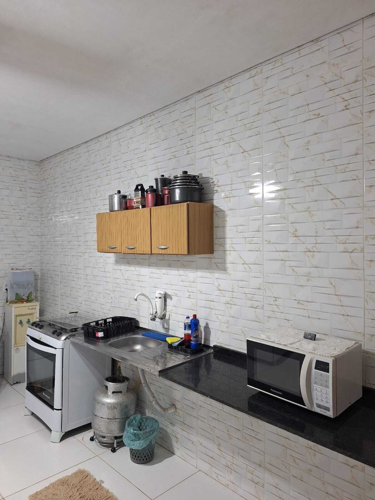 Una cocina con estufa a gas, microondas, lavamanos y alacenas.