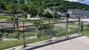 A balcony with a view of a green hillside, a body of water, and buildings in the distance.