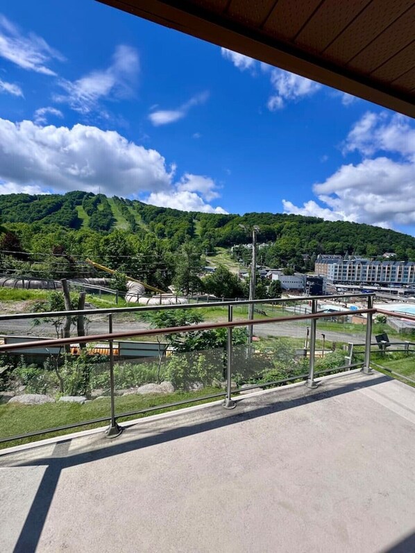 A balcony with a view of a green hillside, a body of water, and buildings in the distance.