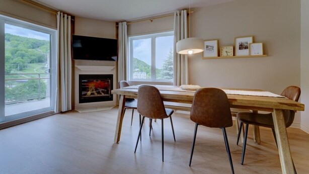 A dining area with a fireplace, large windows, and a view of greenery.