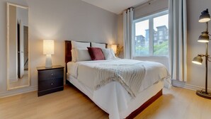 A bedroom with a bed, bedside table, lamp, and a window with curtains.