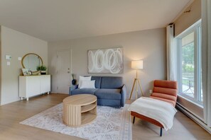 A modern living room with a sofa, a round coffee table, a side table, a floor lamp, and a window with a view.