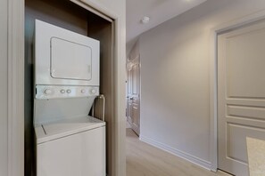 A laundry room with a washer and dryer, a radiator, and a hallway leading to a door. - E201-Condo ski in ski out ~velo in velo out (Bromont)
