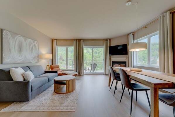 A modern living room with a sofa, coffee table, dining table, chairs, a fireplace, and a TV.